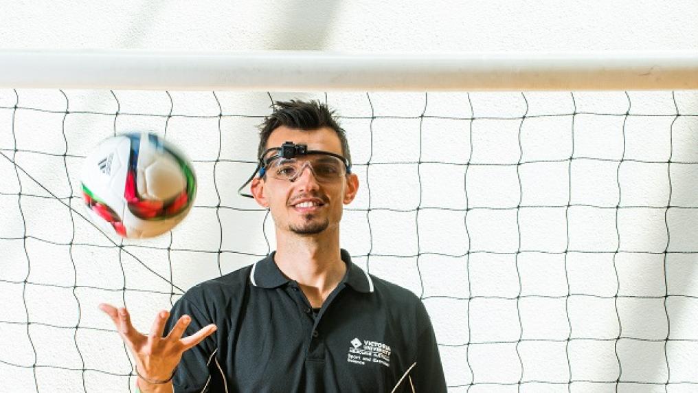 Luca Oppici throwing a soccer ball in the air, with a net behind him