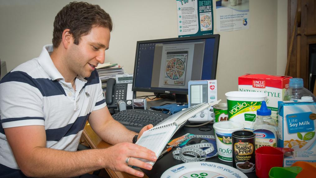 Master of Nutrition student at a computer desk with different foods and charts