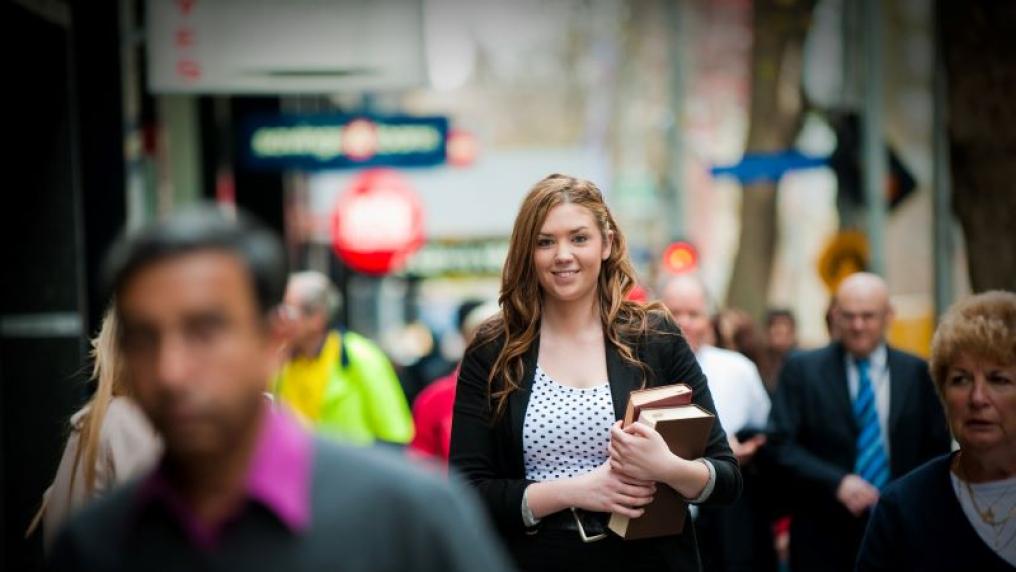 Student in busy city lane holding books and dressed professionally