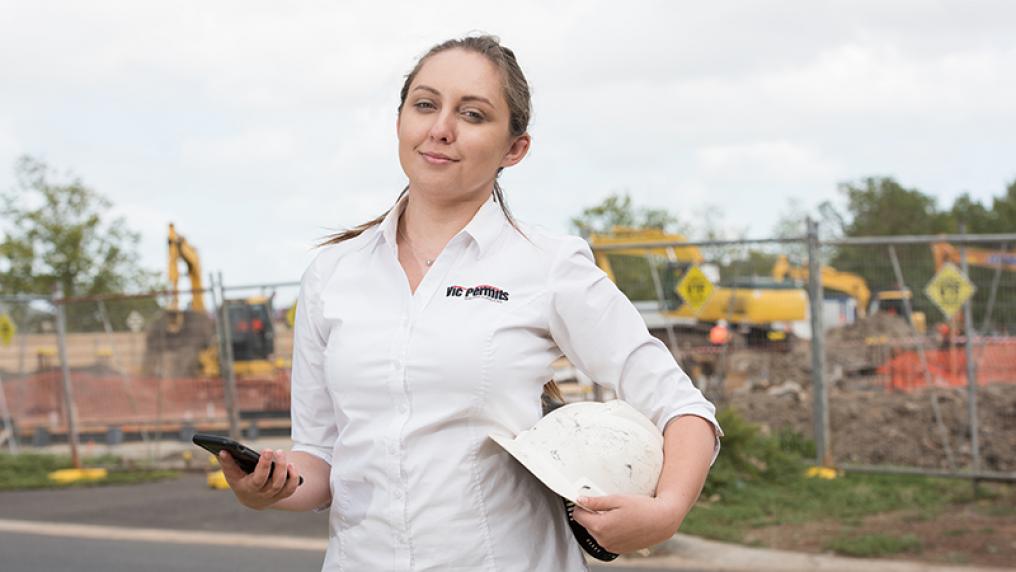 Violetta Jakielaszek in front of a construction site holding a hard hat and a mobile phone