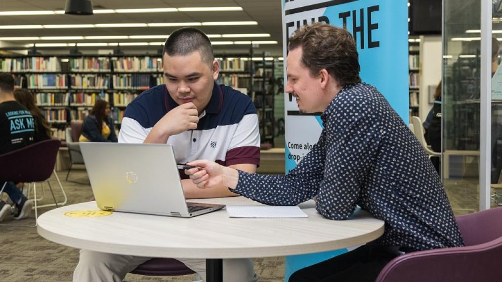 Student mentor with student in library, explaining something on a laptop
