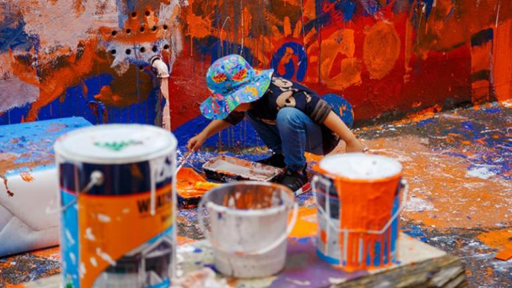 toddler painting an outdoor wall in bright colours