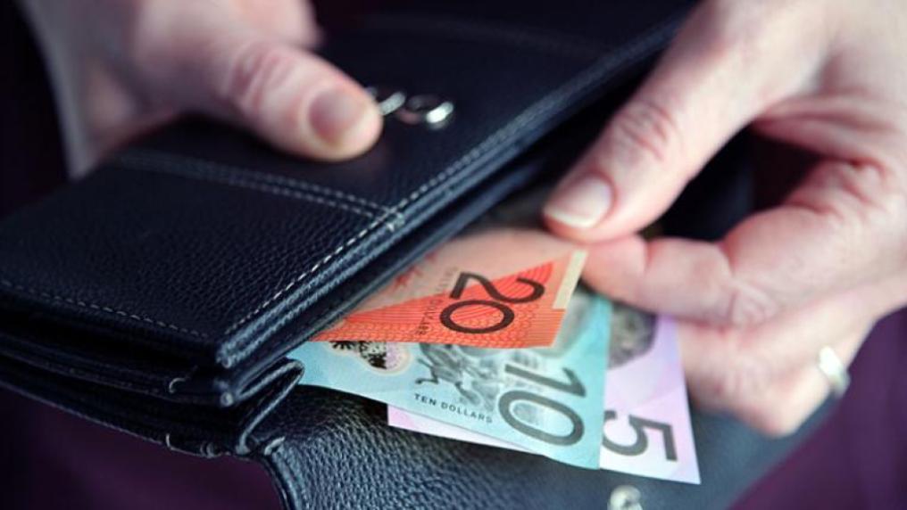 A hand pulling a $20, $10 and $5 note out of a wallet.