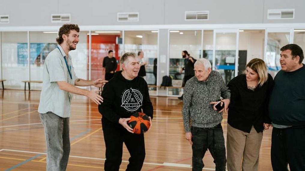 A young man assisting a group of adults with disability to play basketball