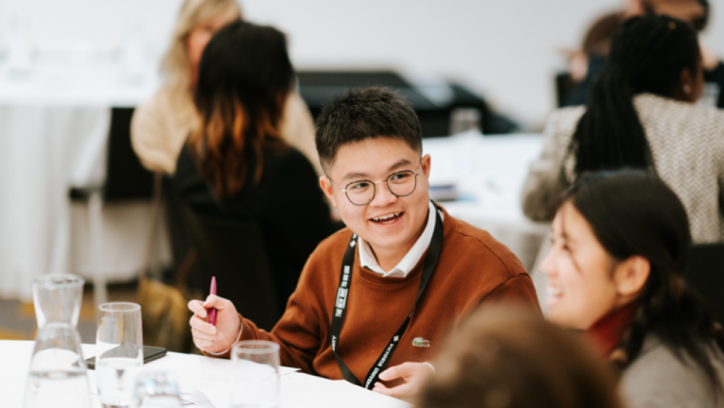 A male student engages with other students at the table at the 2023 Student Leadership Conference