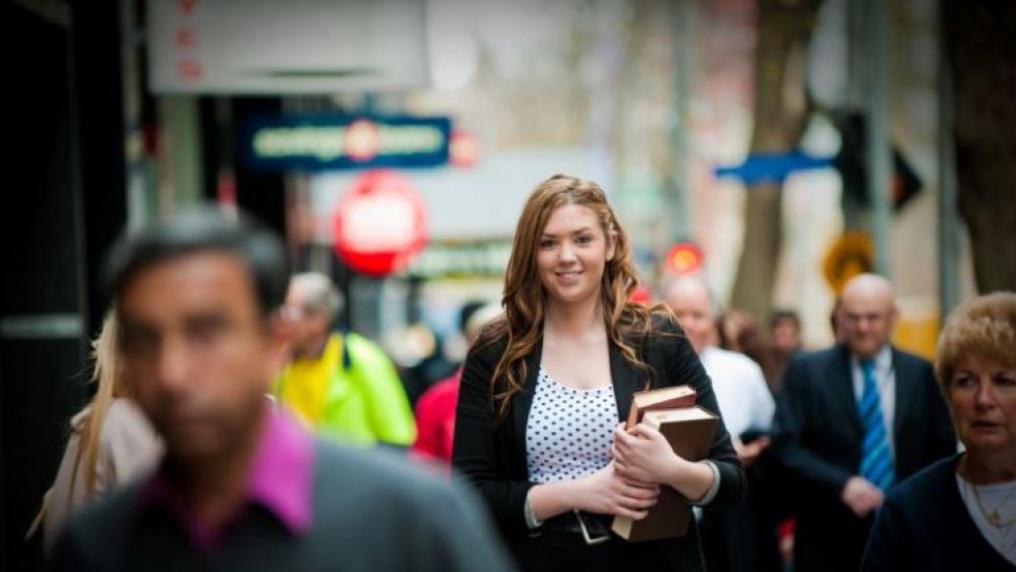 Student in busy city lane holding books and dressed professionally