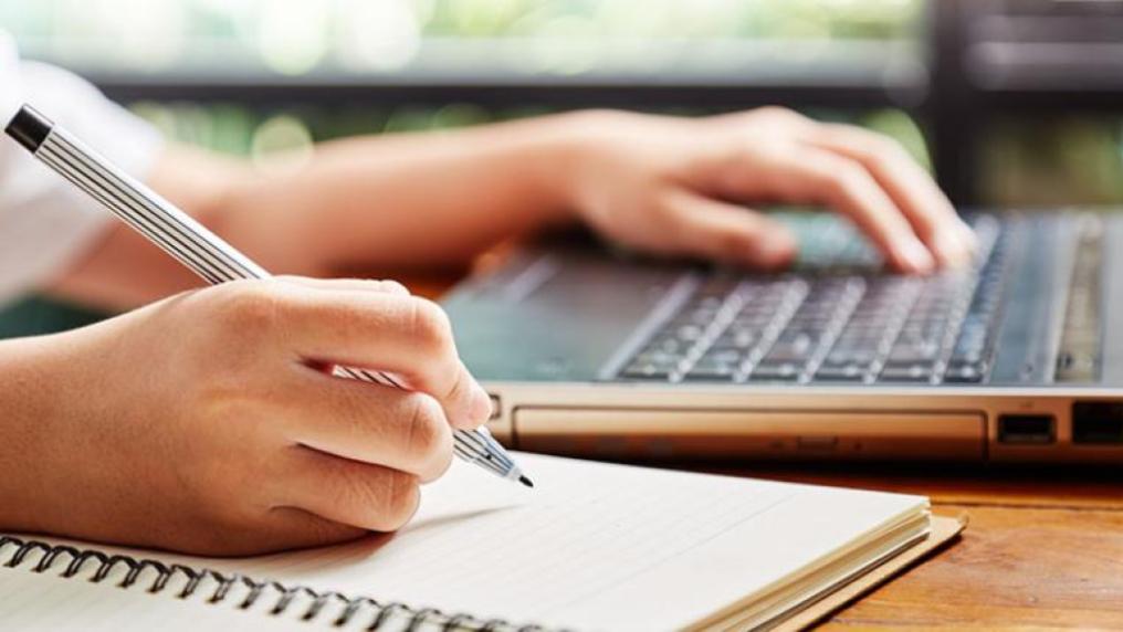 A student writes notes off a laptop while studying.