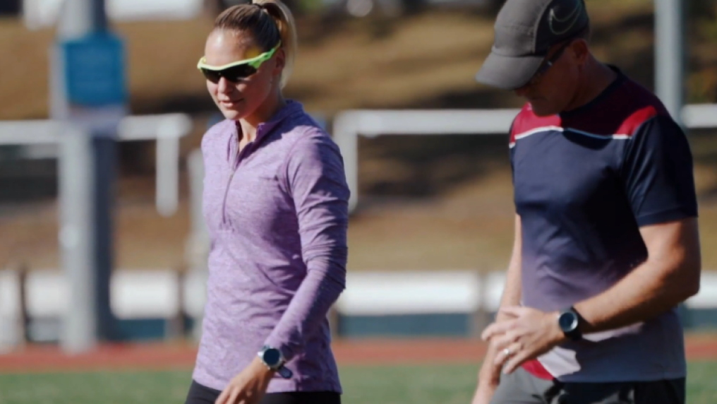 Woman on sport field in sport attire wearing dark glasses, with man in sport attire