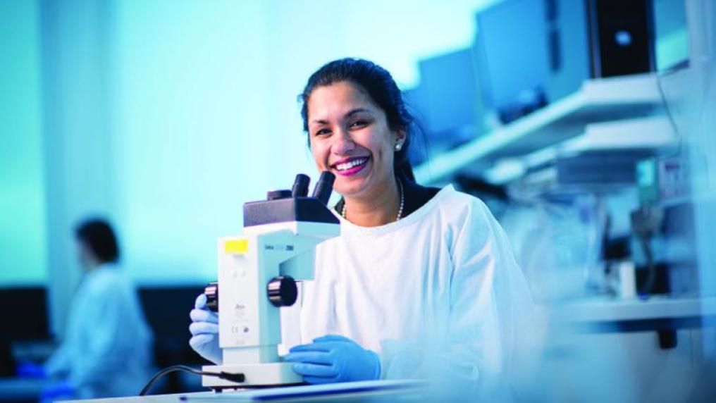 A female researcher in lab-coat and gloves at a microscope in a lab.