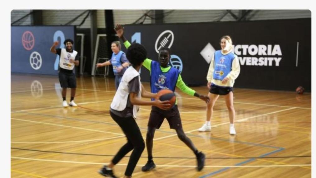 A multicultural group of teenage boys play basketball with VU students